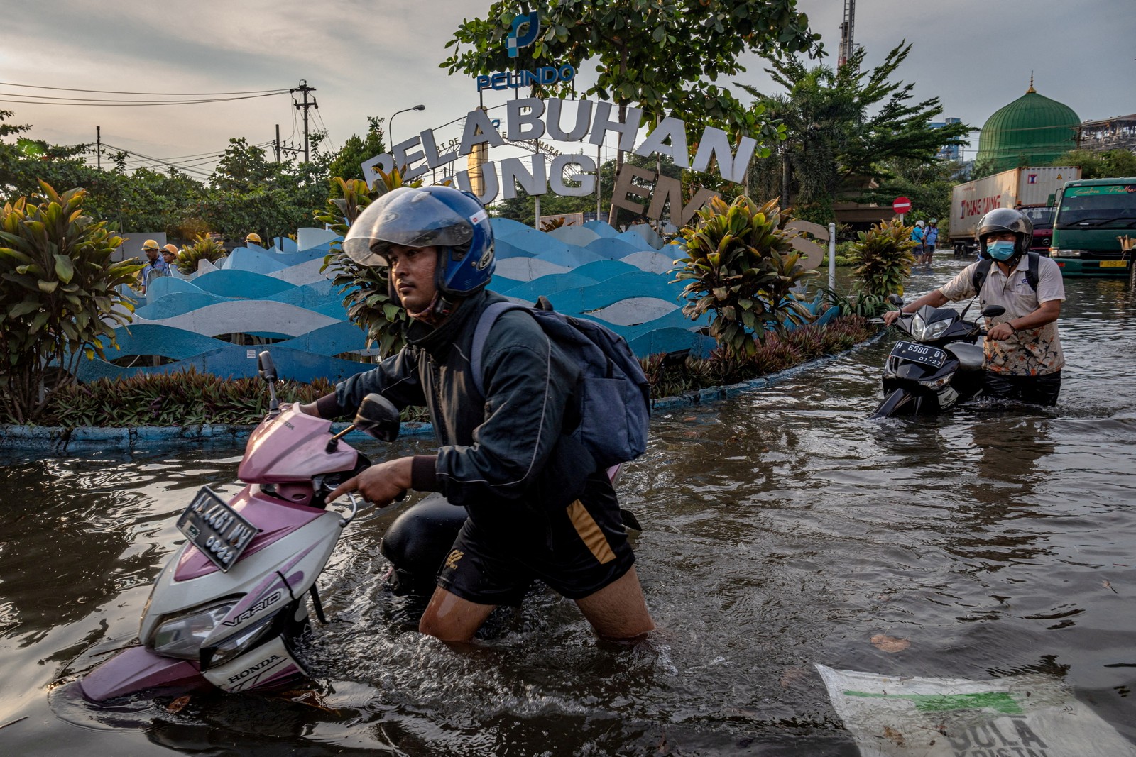 Trabalhadores empurram suas motos por área inundada do terminal portuário de Tanjung Emas, após marés altas e quebra-mares, em Semarang, província de Java Central, Indonésia  — Foto: ANTARA FOTO / via REUTERS