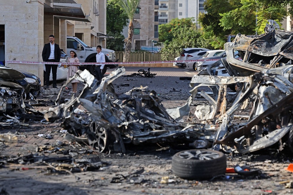 Moradores observam os destroços de veículos destruídos em Ashkelon após um ataque de foguete da Faixa de Gaza ao sul de Israel em 7 de outubro de 2023 — Foto: AHMAD GHARABLI / AFP