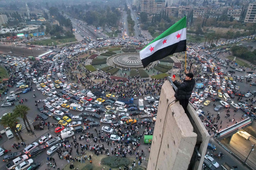 Homem ergue bandeira rebelde síria na Praça Umayyad, em Damasco — Foto: Bakr Alkasem/AFP