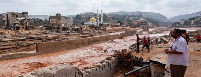 As pessoas olham para os danos causados ​​pelas inundações estranhas em Derna, no leste da Líbia — Foto: AFP