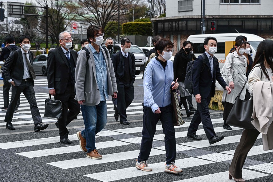 Pessoas atravessam uma rua no centro de Tóquio, no primeiro dia de redução dos requisitos de máscara. - O governo do Japão facilitou suas diretrizes de máscara em 13 de março, recomendando-as apenas em trens lotados e em hospitais ou lares de idosos, mas havia poucos sinais de que os residentes desejavam desmascarar. Foto: Richard A. Brooks / AFP