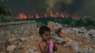 Uma criança em meio aos incêndios que atingem a vila de Agios Charalabos, perto de Atenas. — Foto: Aris MESSINIS / AFP