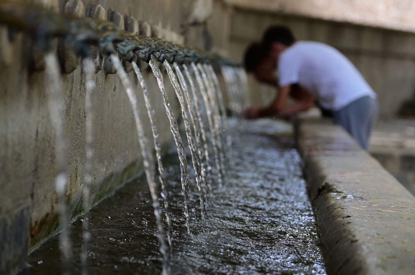 Jovens bebem água em uma fonte em Xativa, ao sul de Valência, em 10 de agosto de 2023, enquanto o país enfrenta a terceira onda de calor do verão, com 44,6 ºC registrados em Sevilha e 43 ºC na região de Valência. — Foto: JOSE JORDAN / AFP