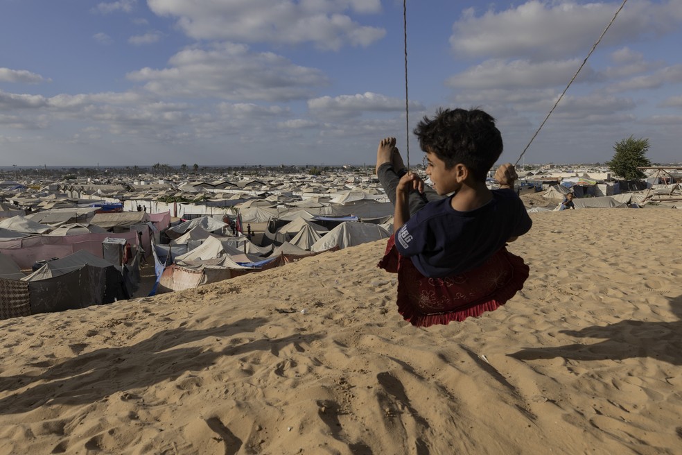 Khan Younis: criança se balança num campo acima do que se tornou a cidade, um imenso campo de refugiados em meio à destruição — Foto: AFP