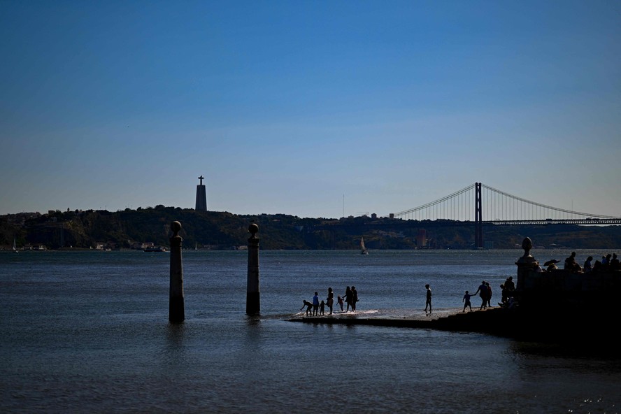 Pessoas caminham pelo Cais das Colunas, na margem do Rio Tejo, em Lisboa