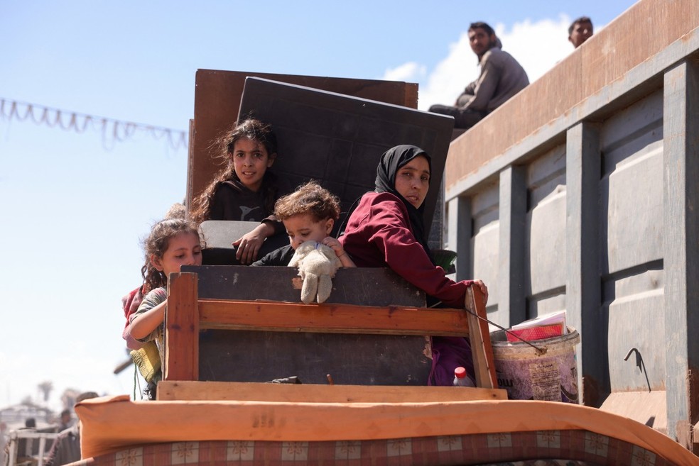 Palestinos carregando pertences chegam a uma trilha costeira a noroeste do campo de refugiados de Nuseirat, enquanto são deslocados para o sul de Gaza após o anúncio israelense de fechar a estrada al-Rashid — Foto: Bashar TALEB / AFP