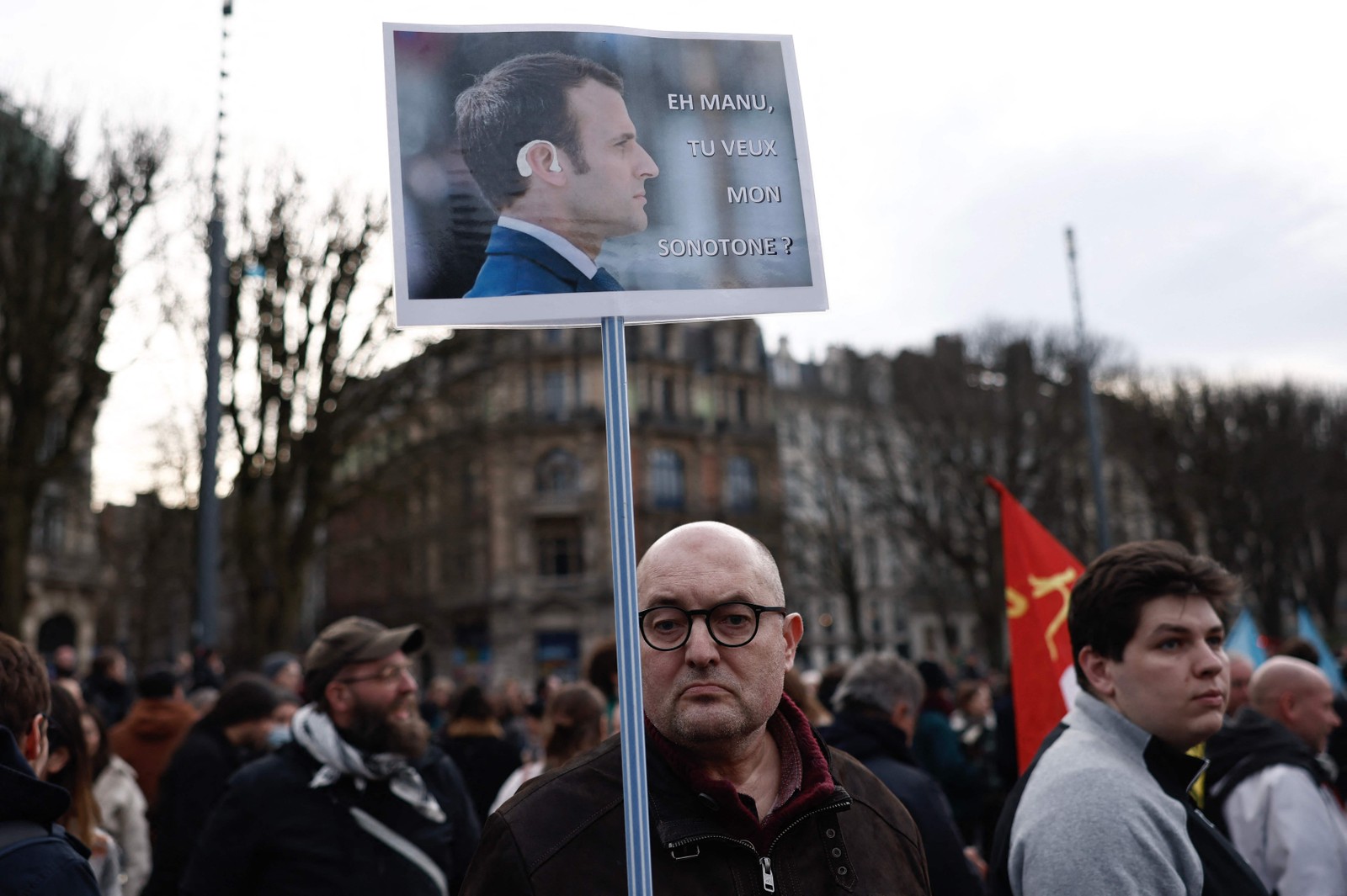 Manifestante segura um cartaz com a foto de Macron e a frase "ei, manu, você quer meu aparelho auditivo?" — Foto: Sameer Al-Doumy / AFP