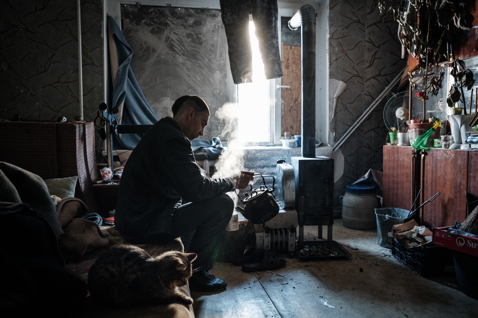 Oleksandr Lugovskykh, 35 anos, que vive sozinho com seu gato, chamado Tyusik, depois que sua família fugiu, prepara uma bebida quente em seu quarto aquecido por um fogão na cidade de Avdiivka — Foto: YASUYOSHI CHIBA / AFP