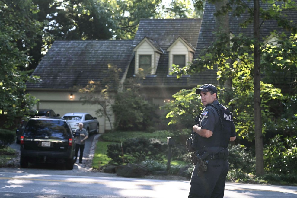 Um policial do condado de Montgomery vigia a casa de John Bolton depois de ação de agentes do FBI, nesta sexta-feira — Foto: PEDRO UGARTE / AFP