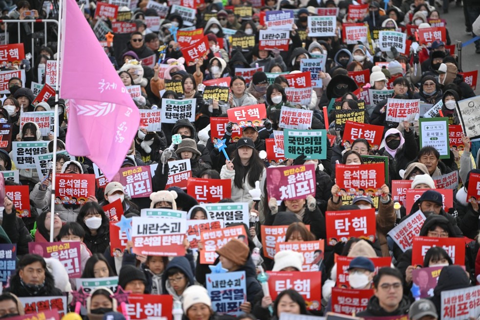 Pessoas seguram cartazes enquanto participam de um protesto pedindo a destituição do presidente da Coreia do Sul, Yoon Suk Yeol, do lado de fora da Assembleia Nacional em Seul — Foto: JUNG YEON-JE/AFP