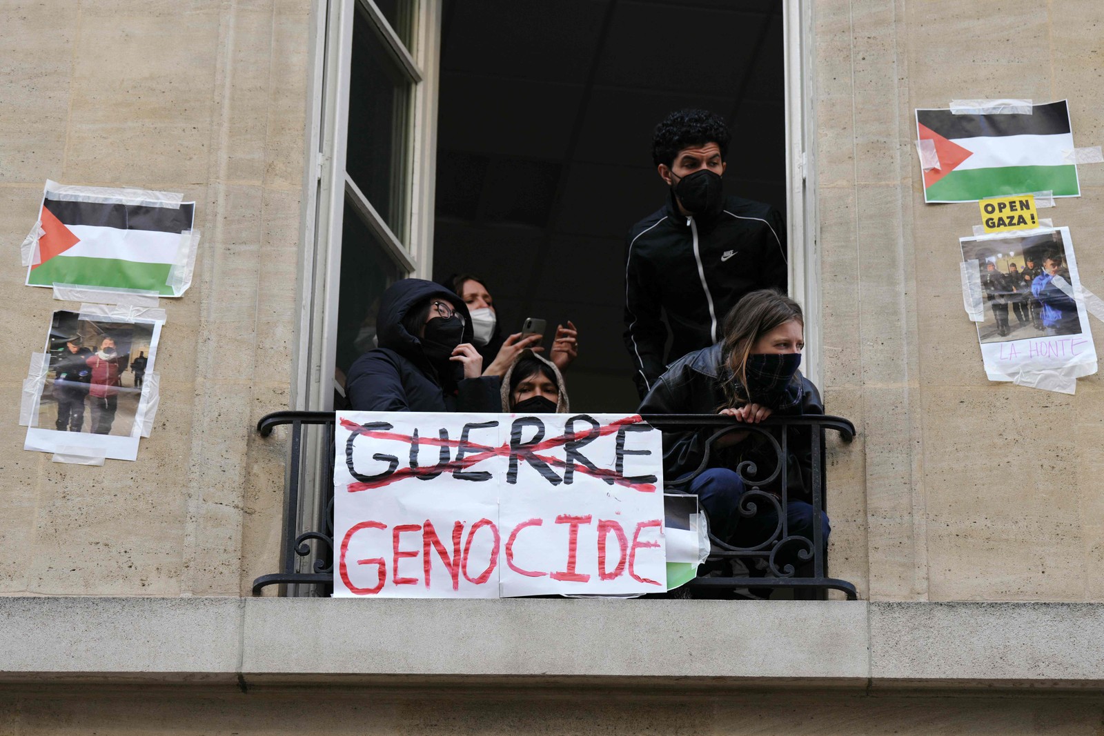 Manifestantes olham pelas janelas durante a ocupação de um prédio do Instituto de Estudos Políticos (Sciences Po Paris) por estudantes em apoio aos palestinos, com uma barricada bloqueando a entrada, em Paris — Foto: Dimitar DILKOFF / AFP