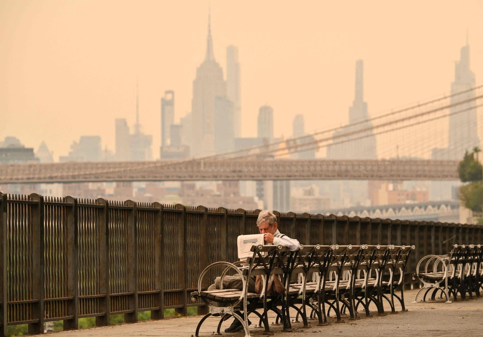 TOPSHOT – Uma pessoa sentada em um banco lê um jornal enquanto a fumaça dos incêndios florestais no Canadá provoca condições de neblina em 16 de julho de 2026, em Nova York. Incêndios florestais fora de controle avançavam na quinta-feira na província canadense de Ontário, provocando evacuações e enviando uma densa fumaça perigosa para os Estados Unidos, onde milhões de pessoas foram expostas a uma qualidade do ar prejudicial à saúde. Estados americanos próximos à fronteira com o Canadá, incluindo Minnesota, Wisconsin, Michigan e Illinois, foram particularmente afetados, enquanto as previsões indicavam que o Nordeste, incluindo Nova York, também continuaria registrando piora na qualidade do ar — Foto: ANGELA WEISS / AFP