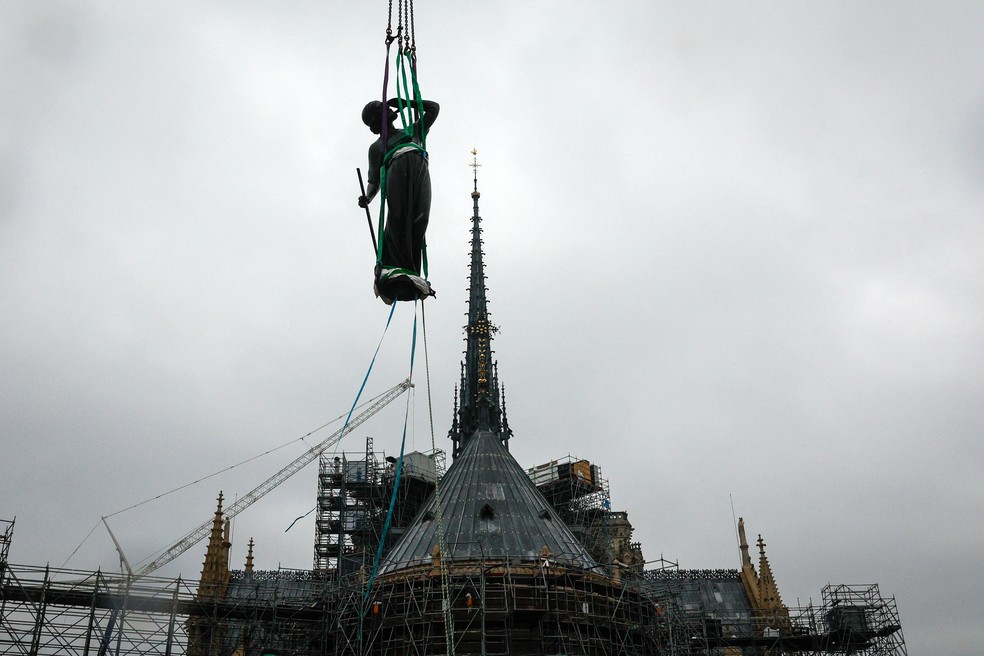 Um guindaste levanta uma estátua de Santo Tomás, a última das 16 gigantes estátuas de apóstolos revestidas de cobre, que serão recolocadas no topo da torre da Catedral de Notre-Dame de Paris — Foto: Geoffroy Van Der Hasselt / AFP
