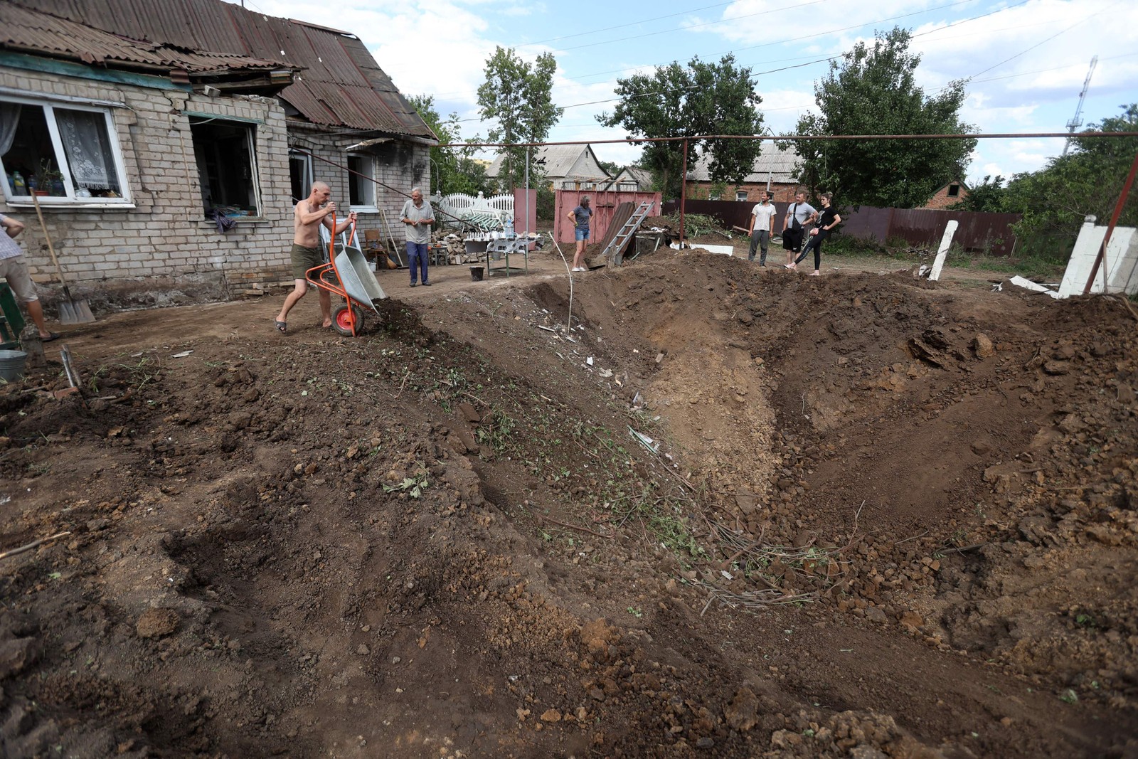 Moradores locais jogam destroços em uma cratera após um ataque russo em Kostyantynivka, região de Donetsk, Ucrânia  — Foto: ANATOLII STEPANOV / AFP