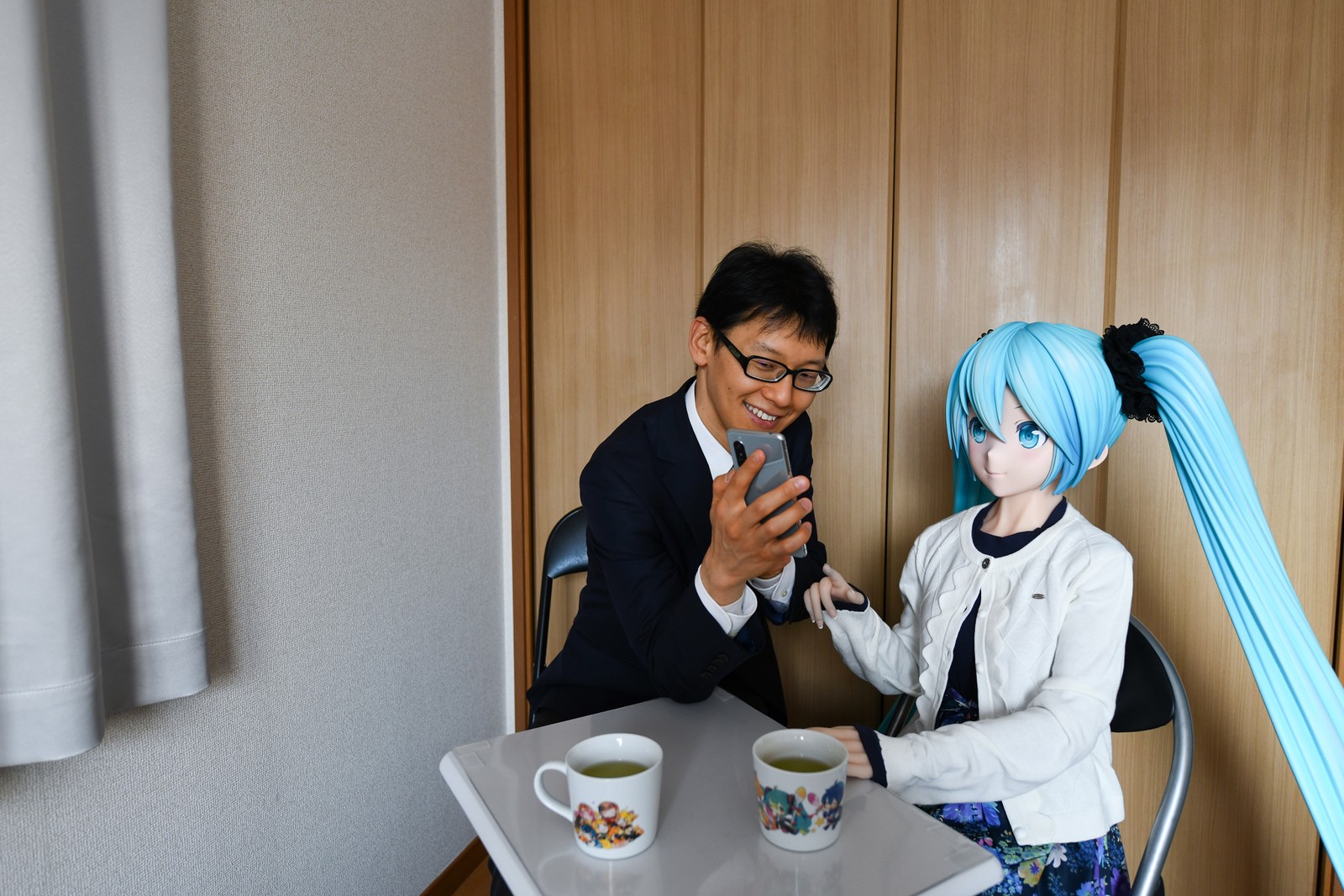 Akihiko Kondo mostra seu telefone para a boneca em tamanho real de Hatsune Miku, a estrela pop virtual, com quem se casou em 2018. Além de Kondo, milhares de outros estão tendo relacionamentos fictíciosNYT