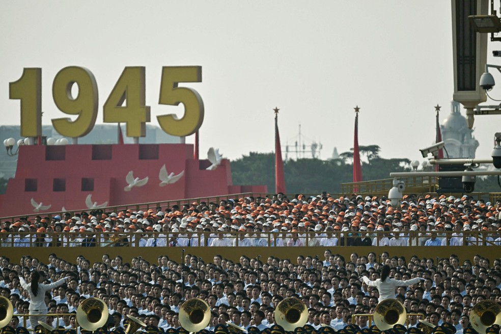 Pessoas cantam ao lado de uma banda militar antes de um desfile militar que marca o 80º aniversário da vitória sobre o Japão e o fim da Segunda Guerra Mundial, na Praça da Paz Celestial, em Pequim — Foto: Pedro Pardo / AFP