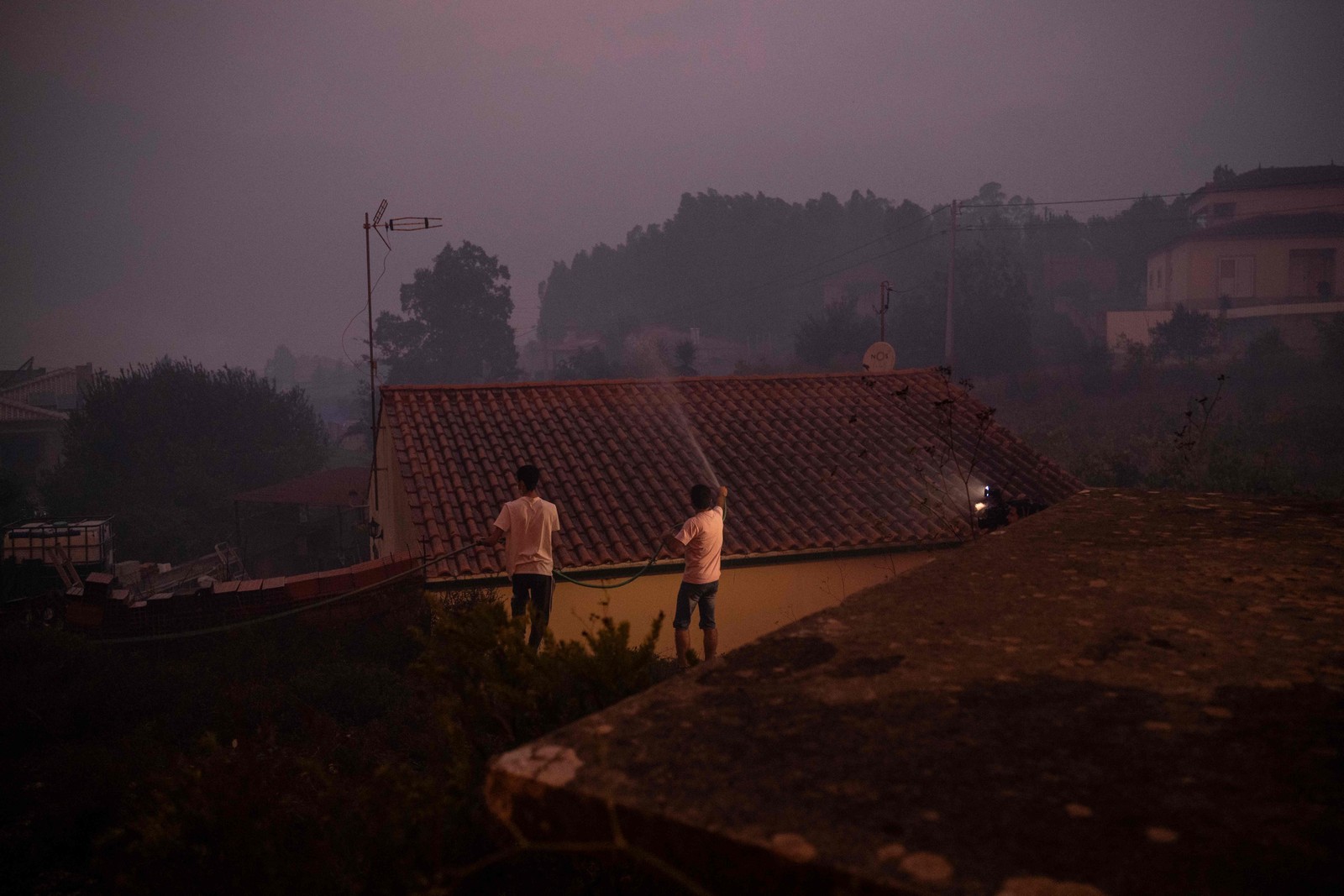 dois homes usam uma uma mangueira parajogaráguasobre o telhado de um casaemágueda -foto: patríciade melo Moreira/afp