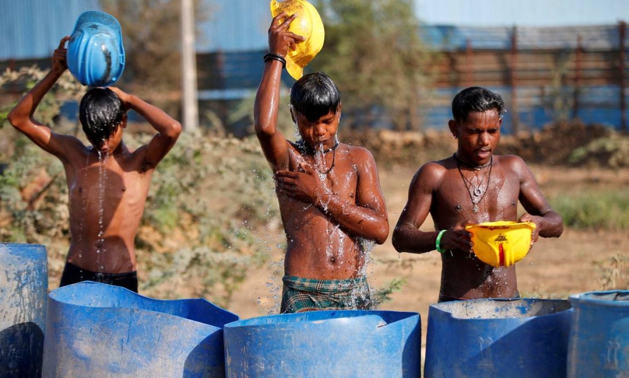 Trabalhadores usam seus capacetes para despejar água para se refrescar perto de um canteiro de obras nos arredores de Ahmedabad  — Foto: AMIT DAVE / REUTERS