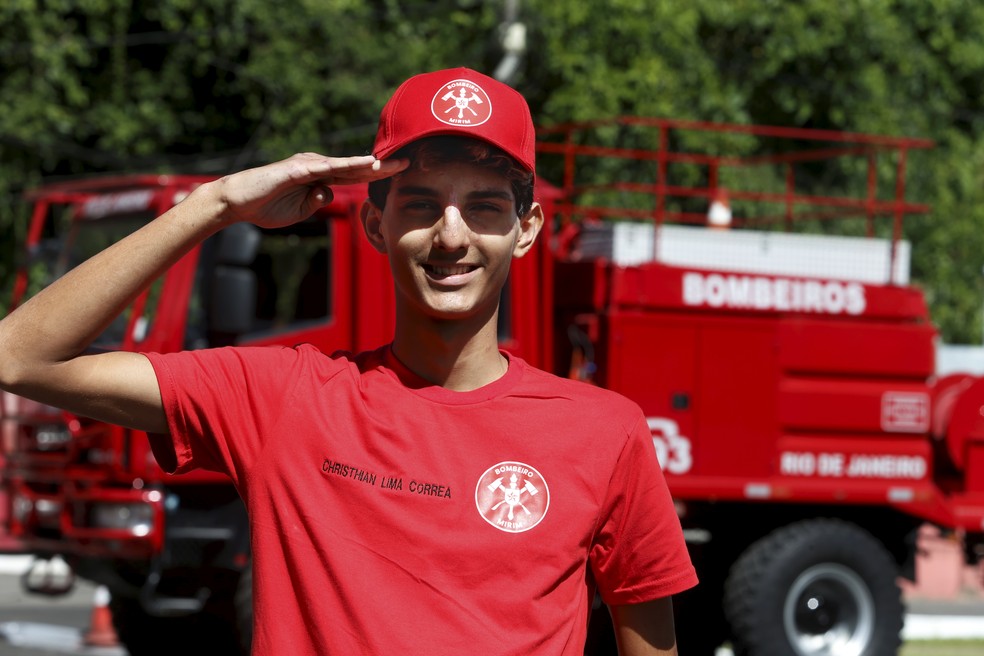 Christhian com a camisa e o boné de bombeiro mirim que ganhou da corporação — Foto: Fabiano Rocha/Agência O Globo