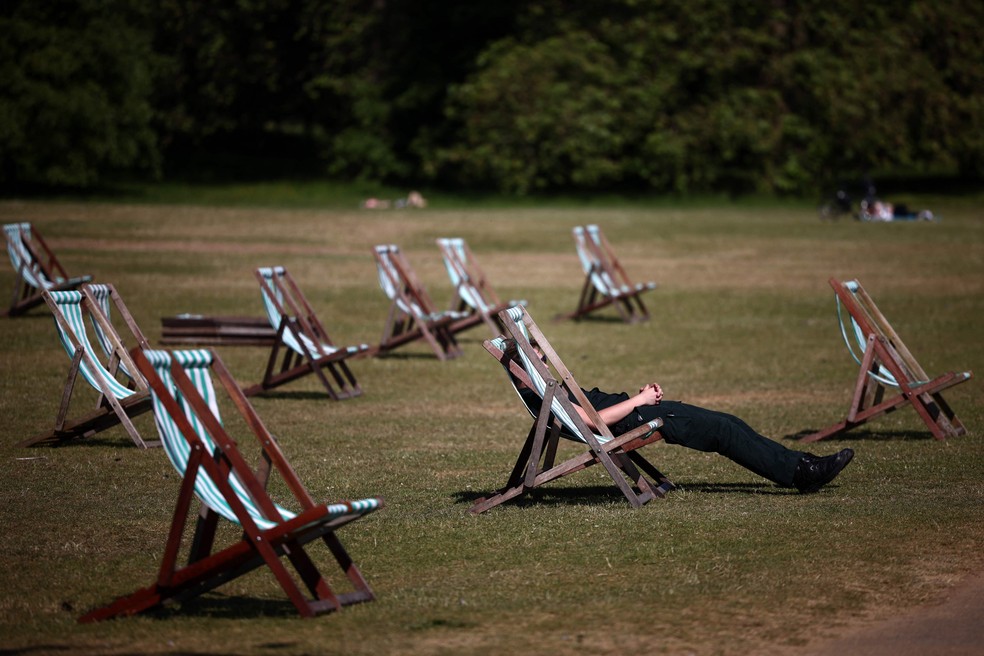 Pessoas se sentam em espreguiçadeiras na grama seca sob o sol no Hyde Park, no centro de Londres. — Foto: Henry Nicholls/AFP