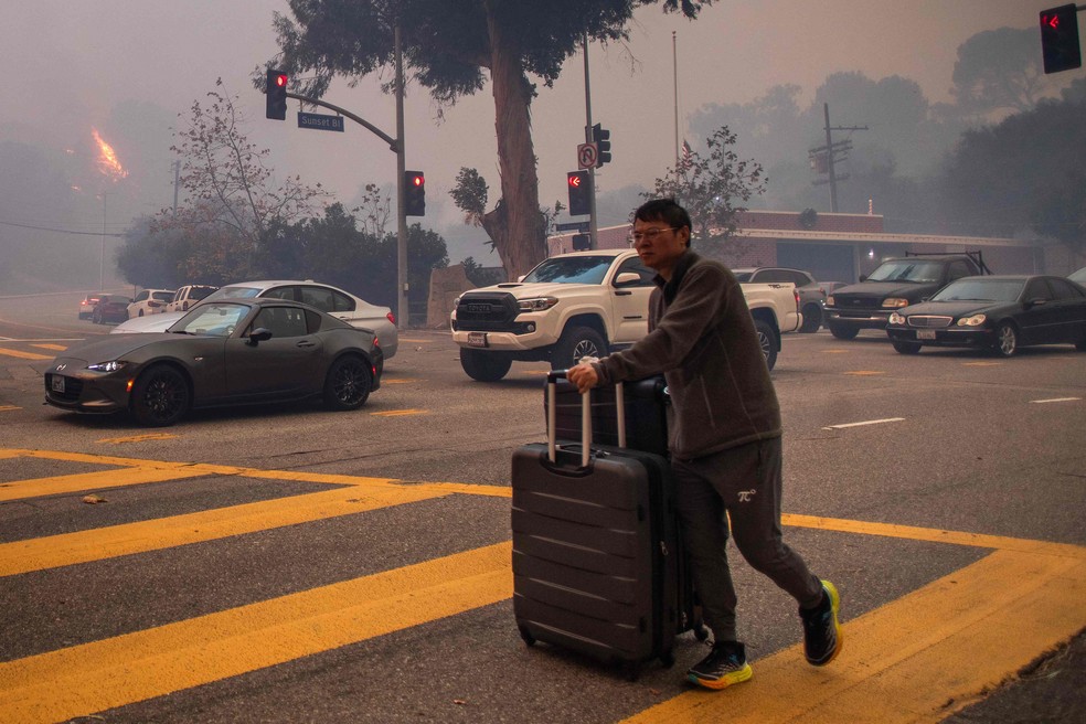 Pela Sunset Boulevard, moradores fogem de carro e a pé do fogo que avança com os fortes ventos na região de Los Angeles — Foto: Apu Gomes/Getty Images/AFP
