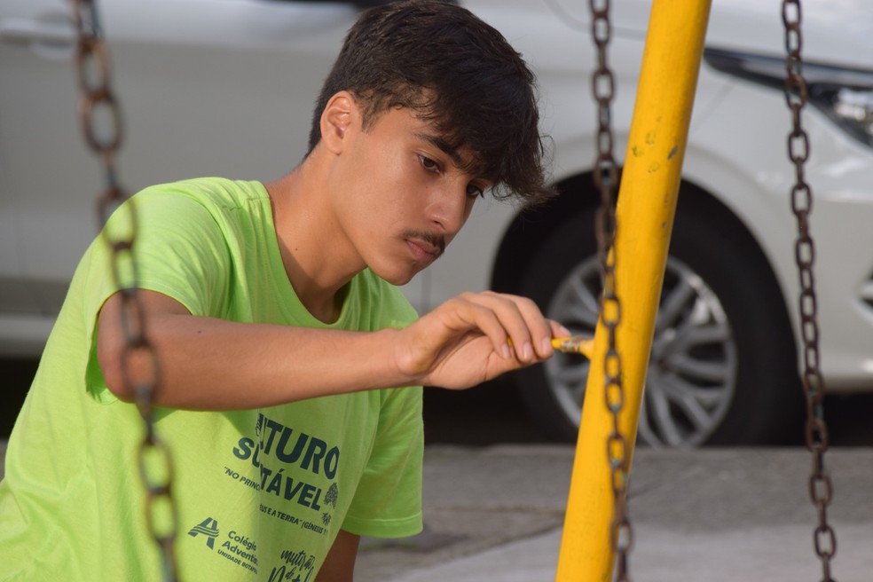 Mão na massa. Com a camisa do novo projeto, Davi Rocha, aluno do 2º ano do ensino médio do Colégio Adventista de Botafogo, pinta o balanço da praça — Foto: Divulgação
