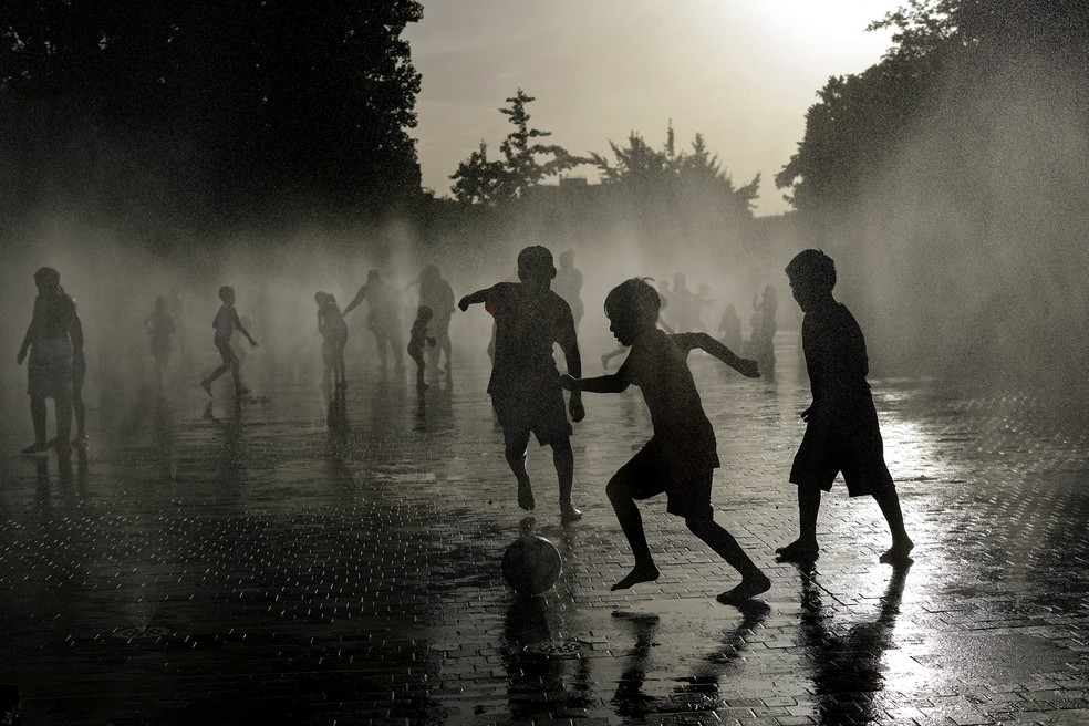 Crianças jogam futebol enquanto se refrescam em uma fonte durante uma onda de calor na Espanha, em Madri, em 23 de junho de 2026 — Foto: Oscar Del Pozo / AFP