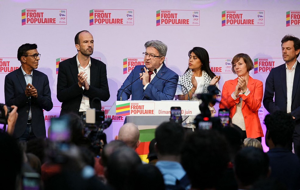 107530870-a-journalist-holds-cards-marked-legislatives-2024-during-the-election-night-of-the-governi ultradireita lidera com 34%, e esquerda avança; Macron pede 'união democrática' no 2° turno