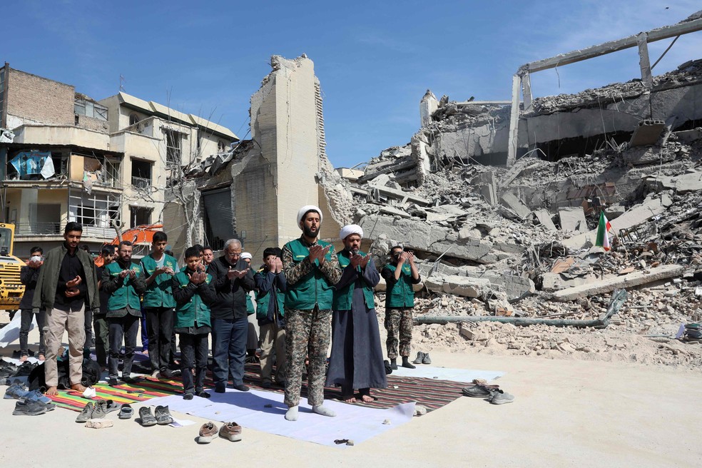 Clérigos e voluntários da Guarda Revolucionária oram ao lado de escombros de uma delegacia destruída em ataques aéreos em Teerã — Foto: AFP