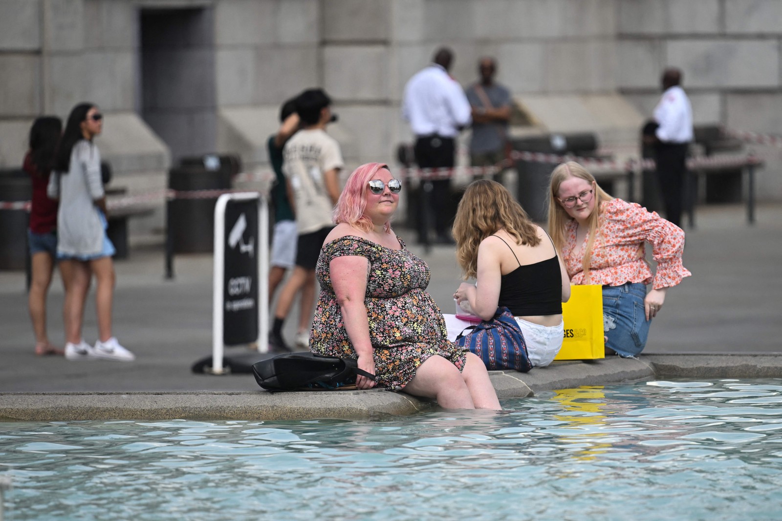 Pedestres se refrescam com os pés na água da fonte de Trafalgar Square, no centro de Londres. A Grã-Betanha emitiu alerta de calor extremo para os próximos dias  — Foto: JUSTIN TALLIS / AFP