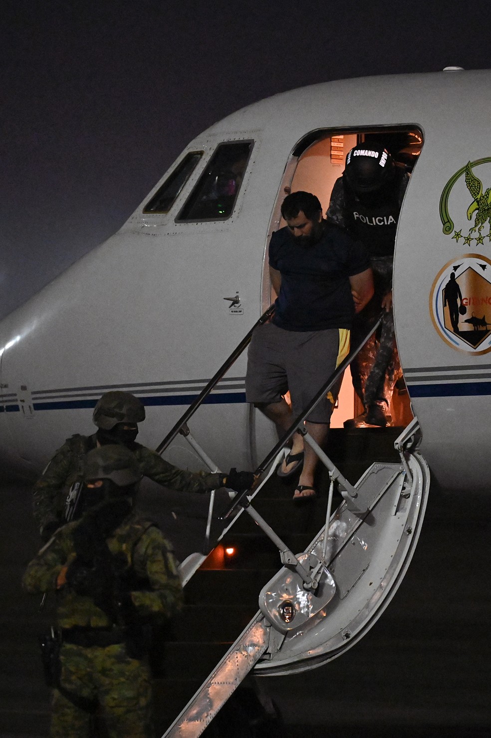 O narcotraficante Adolfo Macías, o Fito (C), é escoltado por militares e policiais ao chegar à base aérea de Guayaquil, no Equador, em 25 de junho de 2025 — Foto: Marcos Pin / AFP