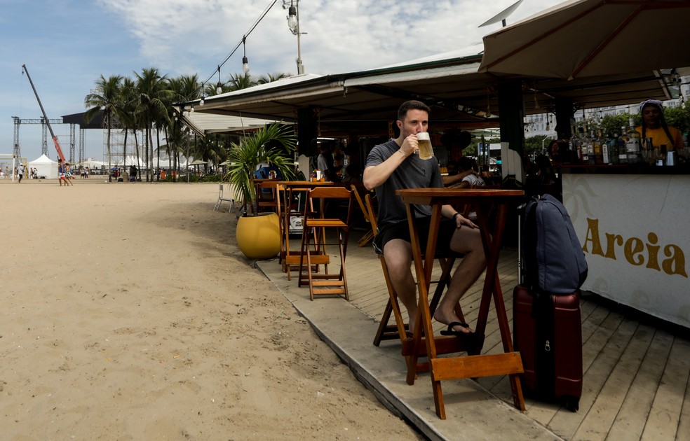Giovane Machado em quiosque, com o palco de Lady Gaga sendo montado ao fundo — Foto: Gabriel de Paiva / Agência O Globo