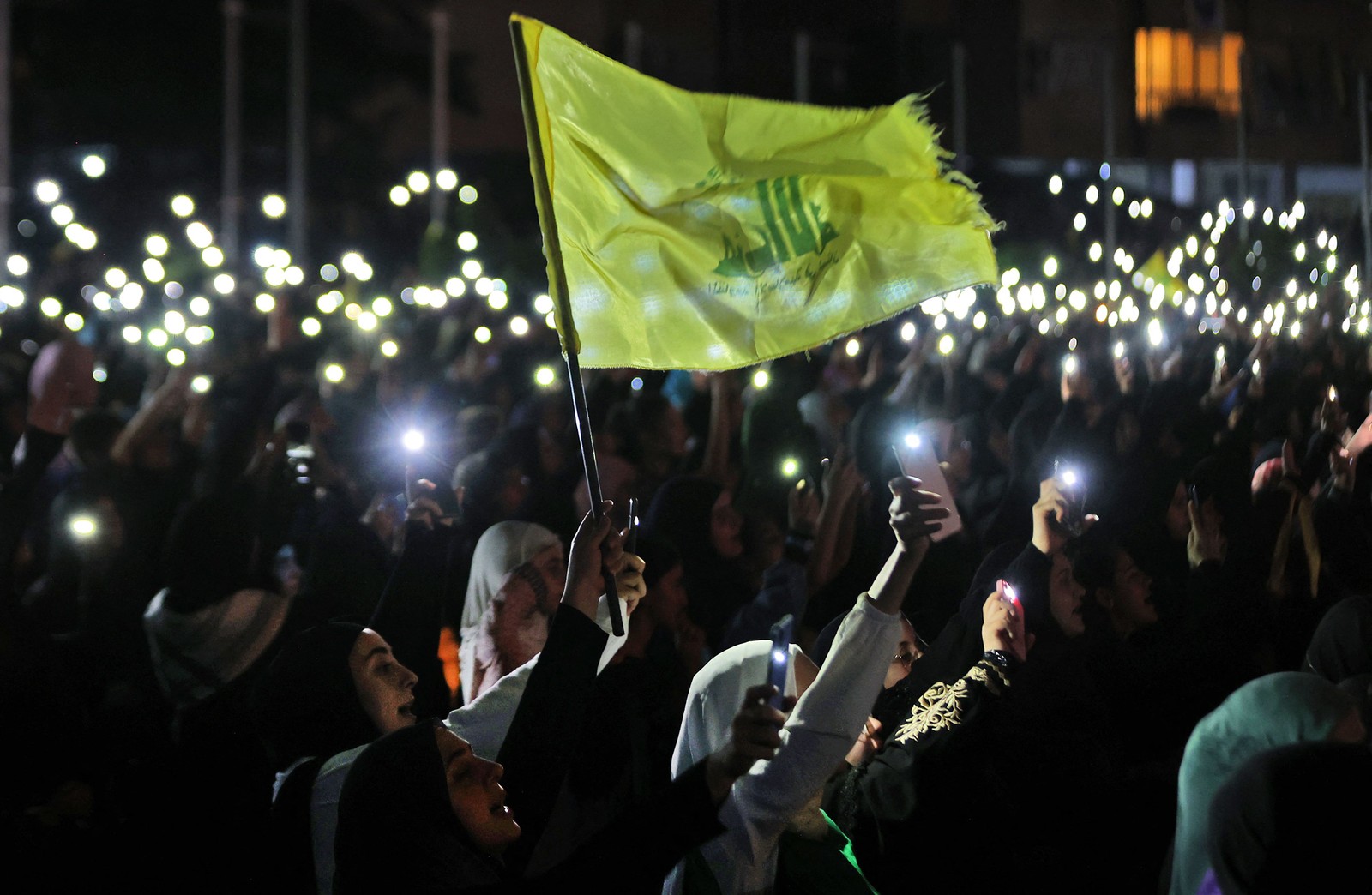 Apoiadores do Hezbollah seguram seus telefones e agitam a bandeira do partido durante uma celebração que marca o 40º aniversário da criação do movimento xiita no subúrbio sul de Beirute  — Foto: ANWAR AMRO / AFP