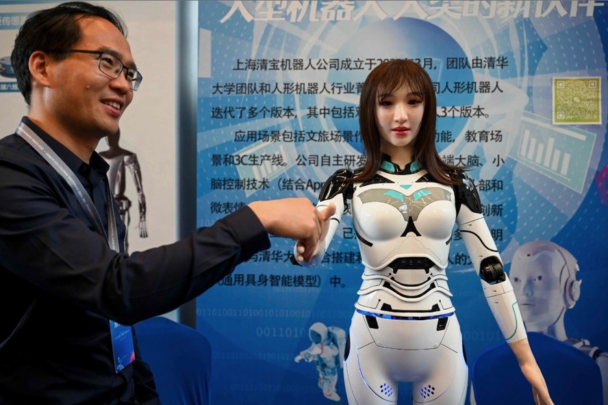 Um expositor aperta a mão de um robô humanoide na Conferência de Desenvolvedores de Robôs Humanoides da China 2024, que acontece em Xangai