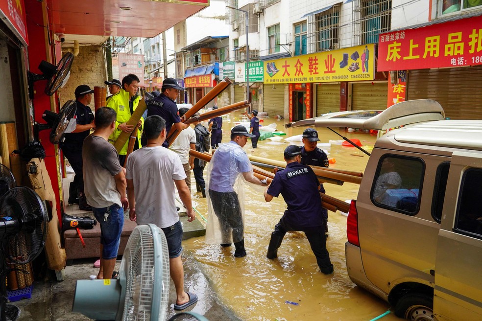 Socorristas ajudam comerciantes a remover equipamentos em uma rua inundada em Congjiang, na região de Guizhou — Foto: AFP