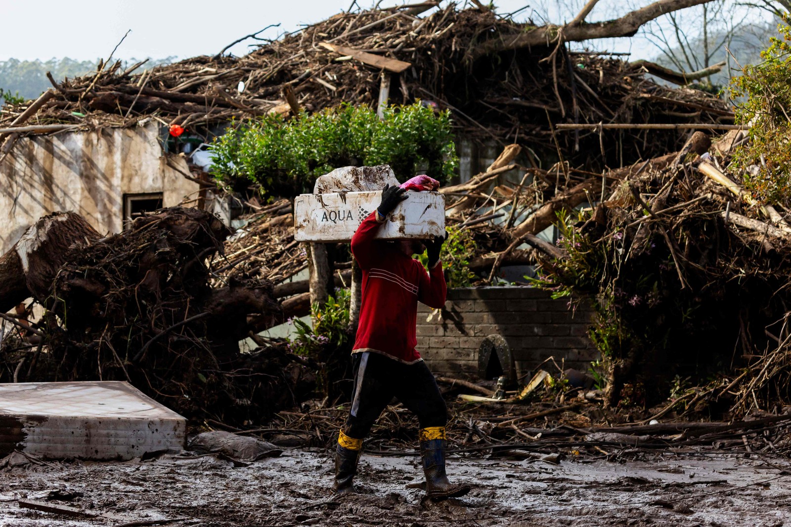 Um homem caminha com seus pertences por uma rua coberta de lama e detritos após um ciclone em Muçum, Rio Grande do Sul — Foto: SILVIO ÁVILA/AFP