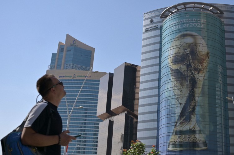 Turista observa imagem do troféu da Copa do Mundo do Catar projetada em prédio de Doha — Foto: Raul ARBOLEDA / AFP