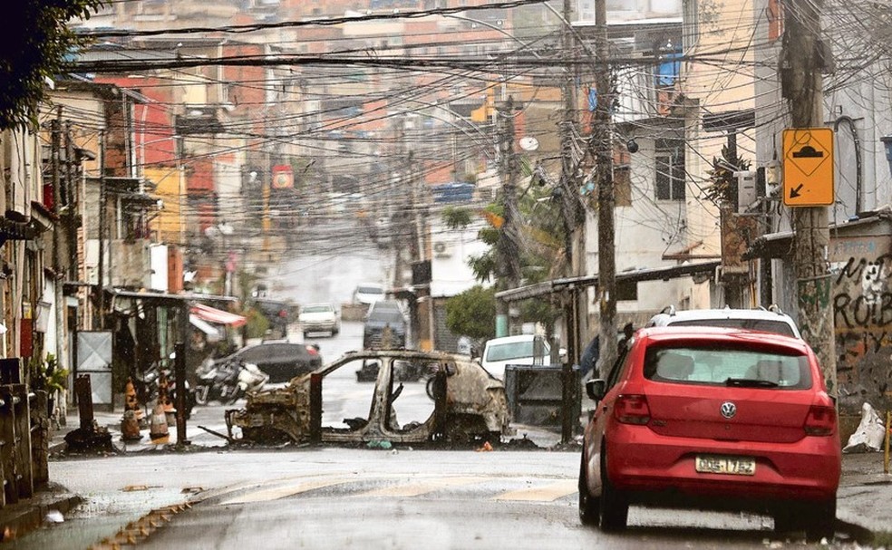 Triste realidade. Carcaça de carro queimado reforça o bloqueio na rua. Três dias depois da megaoperação nos complexos do Alemão e da Penha, barricadas na Vila Cruzeiro mostram que o ir e vir na comunidade segue controlado pelo tráfico — Foto: Fabiano Rocha
