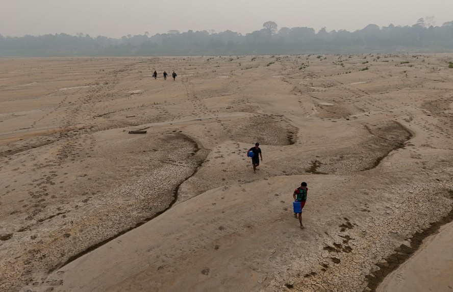 Pessoas caminham sob a areia quente de bancos de areia no leito do Rio Madeira para buscar água em meio à seca mais severa em quase 60 anos