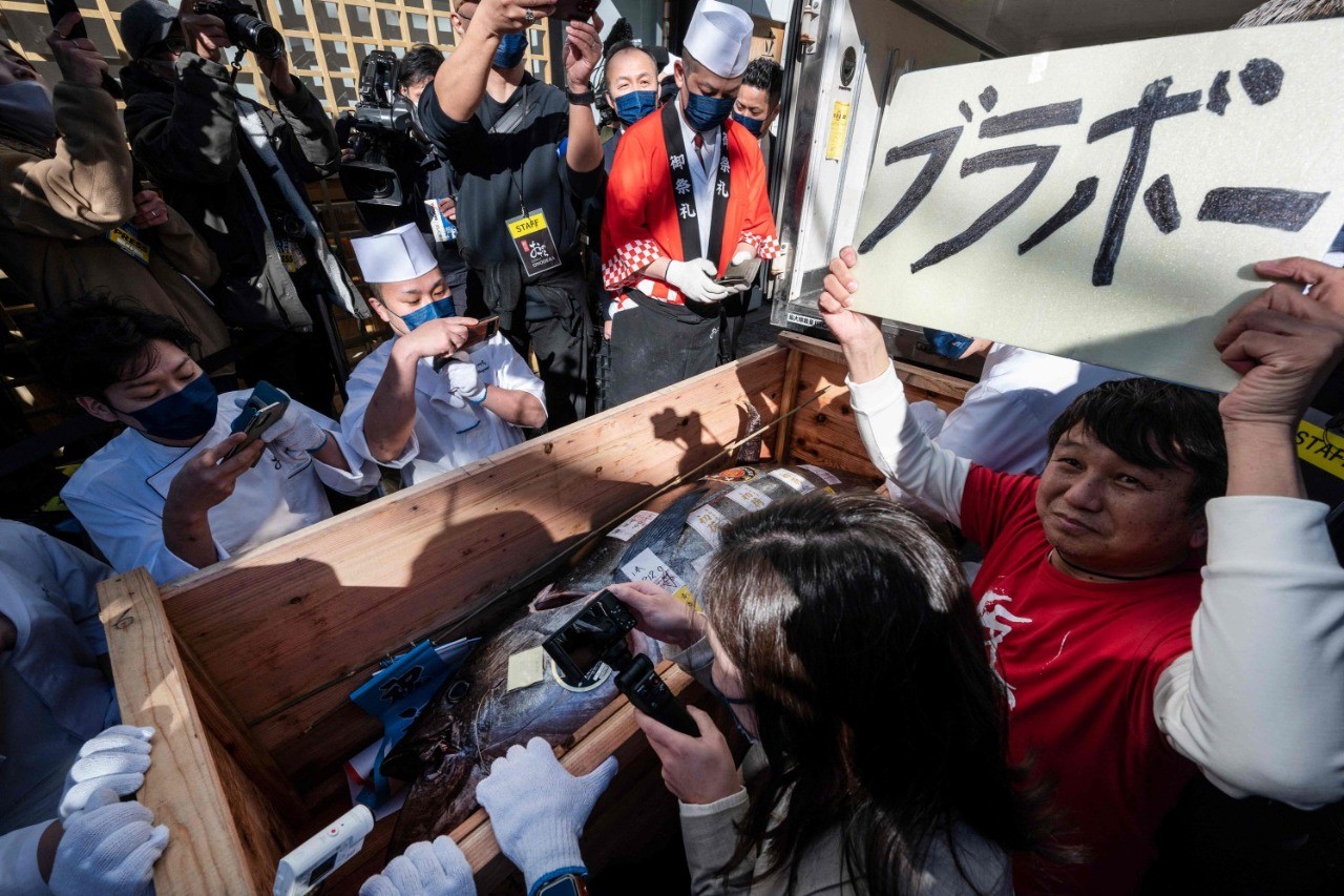 Um homem segura uma placa com a inscrição "bravo" enquanto uma caixa contendo o atum-rabilho é descarregada do lado de fora do restaurante vencedor do leilão — Foto: Richard Brooks/AFP