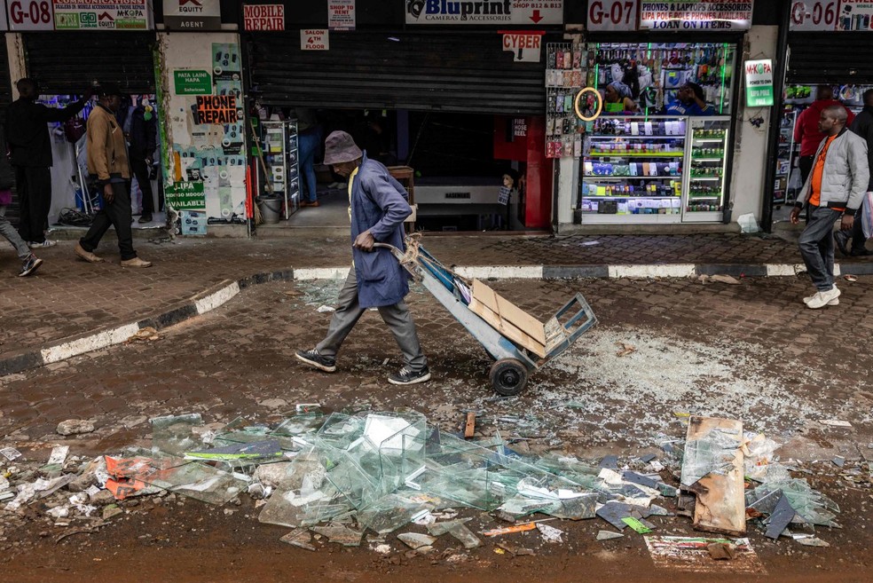 Trabalhador recolhe destroços após loja ser vandalizada durante protesto no Quênia — Foto: Luis Tato / AFP