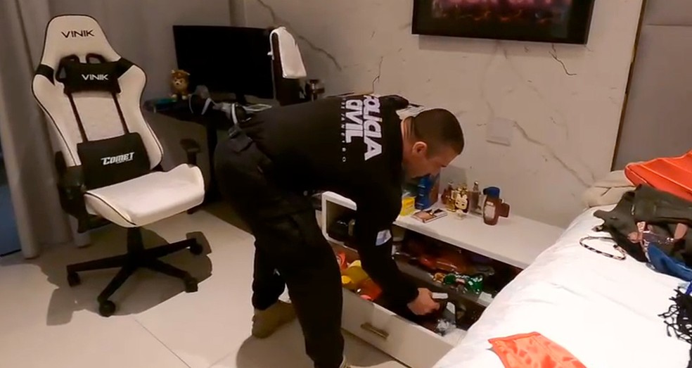 Um policial revista um cômodo de uma residência — Foto: Reprodução