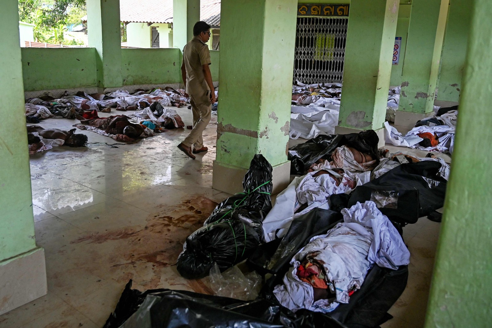 Policial caminha em meio a corpos de vítimas da colisão de três trens, em uma escola de ensino médio usada como necrotério temporário perto de Balasore — Foto: DIBYANGSHU SARKAR / AFP