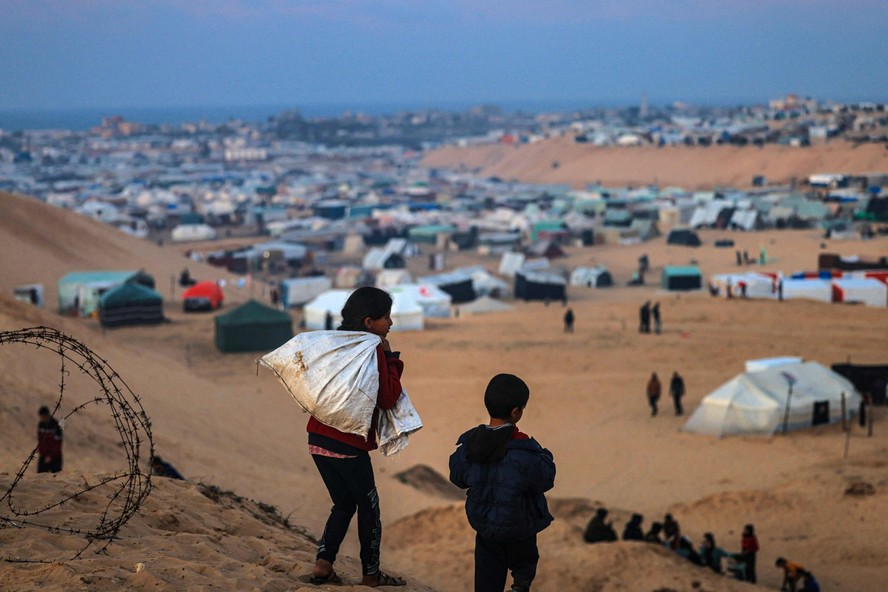 Crianças palestinas deslocadas caminham em uma colina em frente ao seu acampamento improvisado em Rafah, no sul da Faixa de Gaza, na fronteira com o Egito