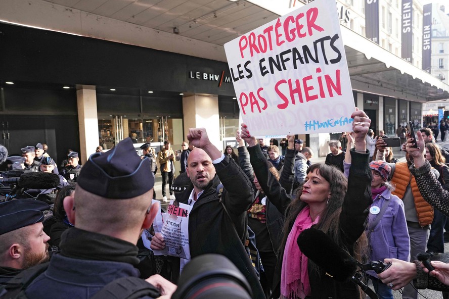 Mulher segura placa onde está escrito 'Proteja as crianças, não a Shein' em meio a protesto em frente à loja de departamento Bazar de l'Hotel de Ville (BHV), em Paris, na inauguração da primeira loja física da gigante asiática no mundo.  Na véspera,  a Shein se comprometeu em 'cooperar integralmente' com as autoridades judiciais francesas após denúncias de vendas ilegais de bonecas sexuais com feições infantis, e afirmou estar preparada para divulgar os nomes das pessoas que compraram esses artigos