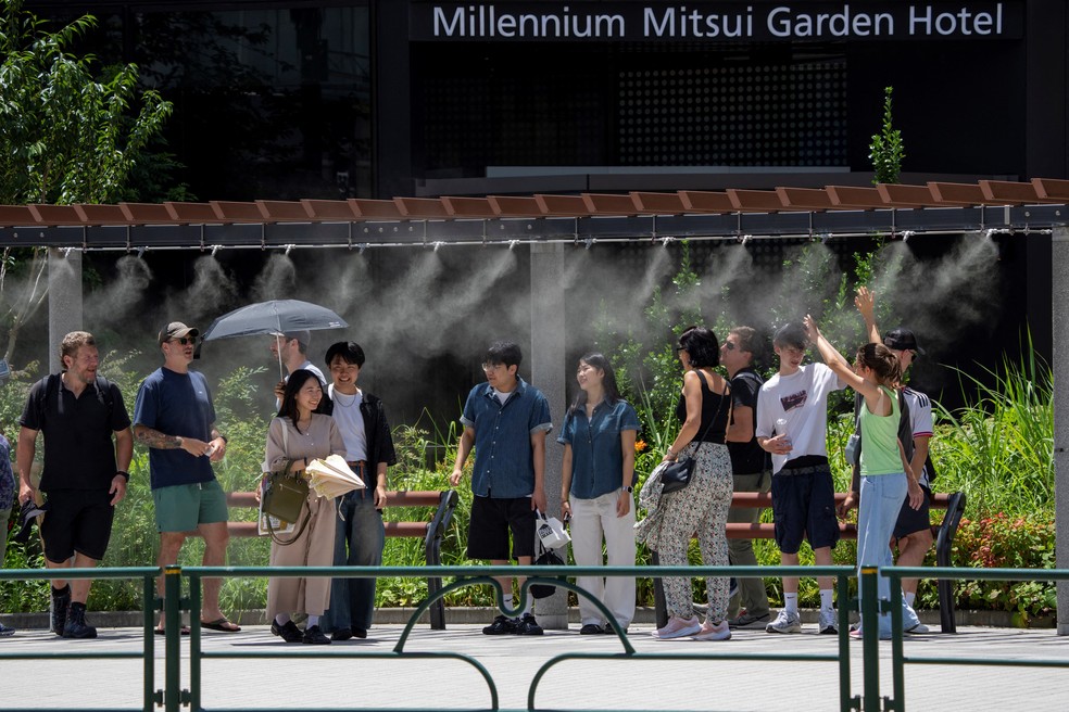 Pessoas descansam sob névoa artificial para se refrescar em um dia quente em Tóquio — Foto: Kazuhiro NOGI / AFP