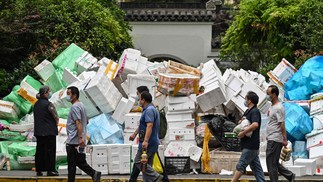 Pessoas passam por caixas empilhadas em uma rua no distrito de Jing'an, em Xangai, após a flexibilização das restrições da Covid-19 na cidade; bloqueio durou dois meses. — Foto: Hector RETAMAL / AFP