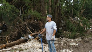 Joe Chavarria procura entre os escombros do acampamento onde cinco parentes desapareceram após a cheia do rio Guadalupe, no Texas — Foto: Jordan Vonderhaar/The New York Times