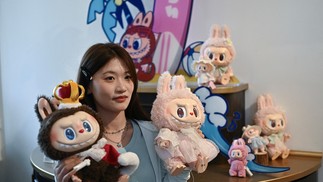 Mulher posando com os personagens Labubu (E) e Mokoko em um salão de exposições enquanto visita o parque temático Pop Land da Pop Mart, em Pequim — Foto: PEDRO PARDO / AFP