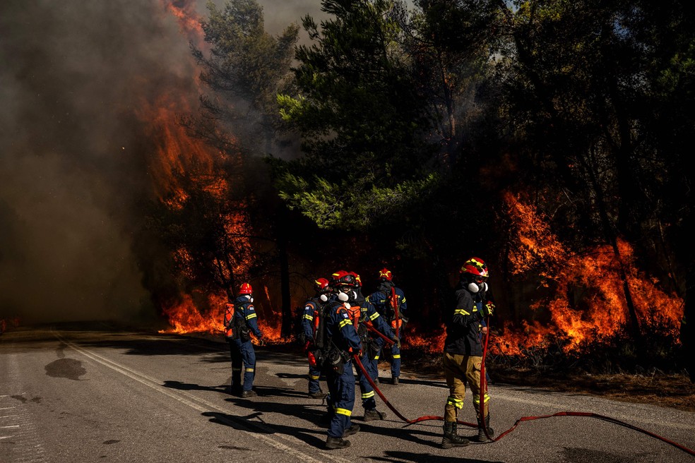 Bombeiros gregos tentam combater um incêndio florestal na região de Porto Germeno, a cerca de 70 quilômetros a noroeste de Atenas — Foto: ANGELOS TZORTZINIS/AFP